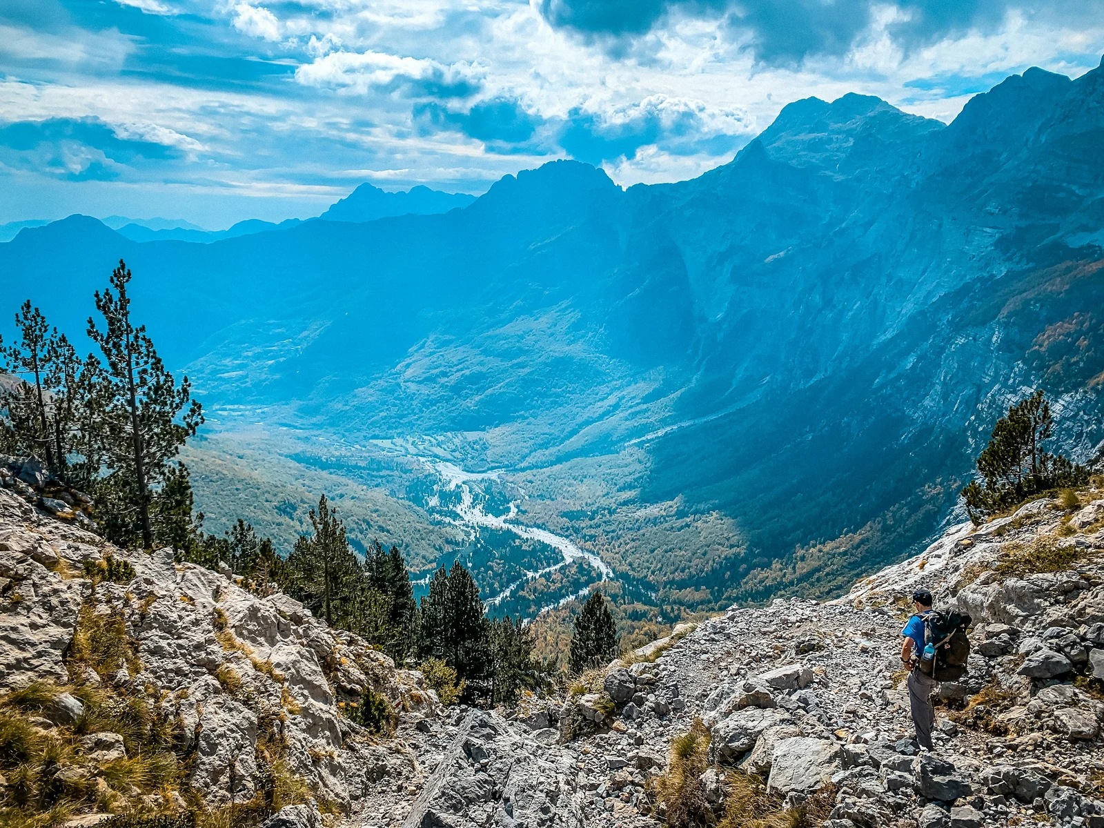 A hiker descending a rocky trail into a mountain valley
