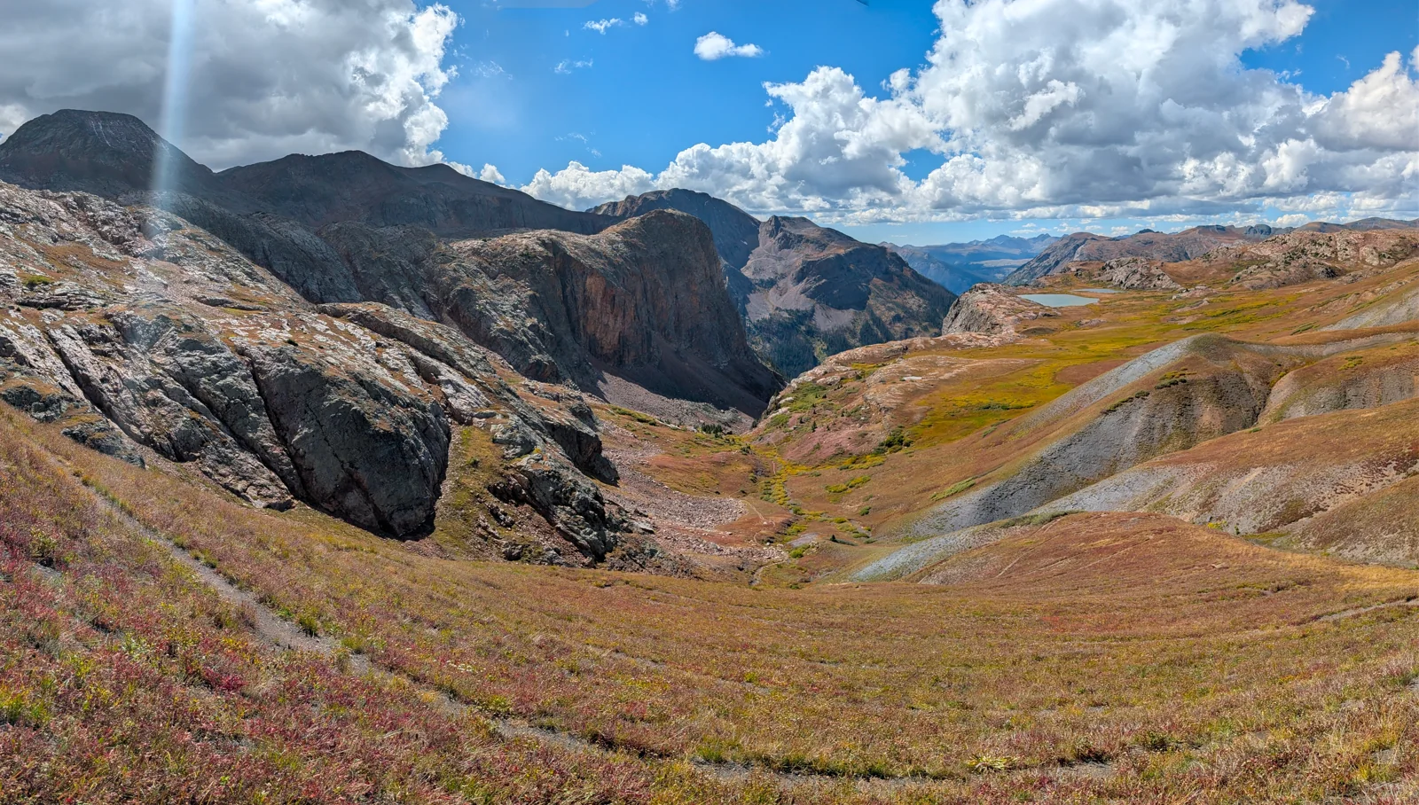 Sunlit mountain ridges and a trail descending through an alpine valley